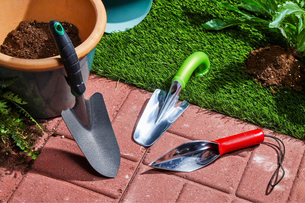 A trowel set arranged on the ground next to a pot half filled with dirt.