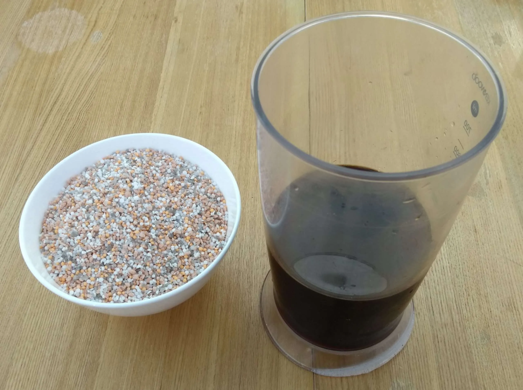 Granular fertilizer in a bowl resting on a table next to a glass container of liquid fertilizer.
