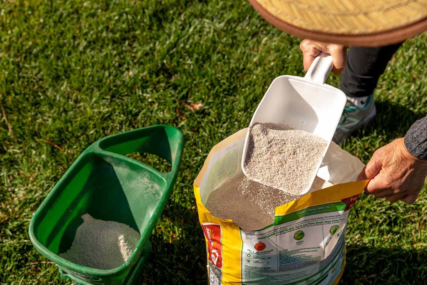 Person scooping lawn fertilizer from a bag into a spreader.