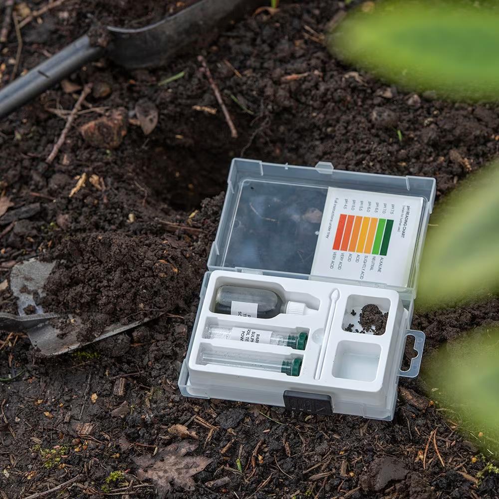 Soil testing kit placed on garden soil with tools for checking pH and nutrients.