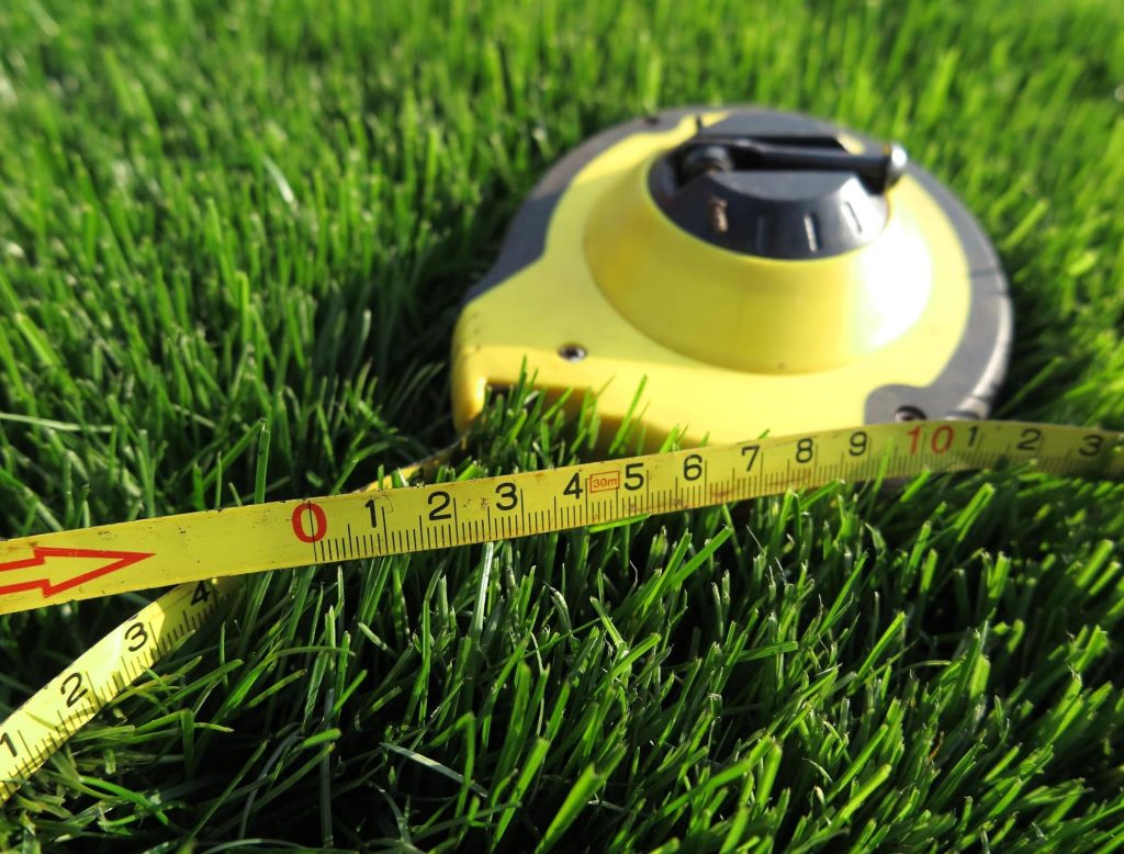Yellow measuring tape and reel lying on lush green grass for lawn measurement