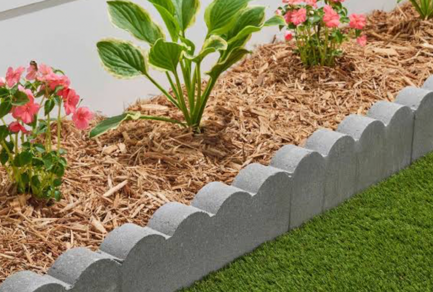 mulched flower bed with concrete scalloped edging and ornamental plants