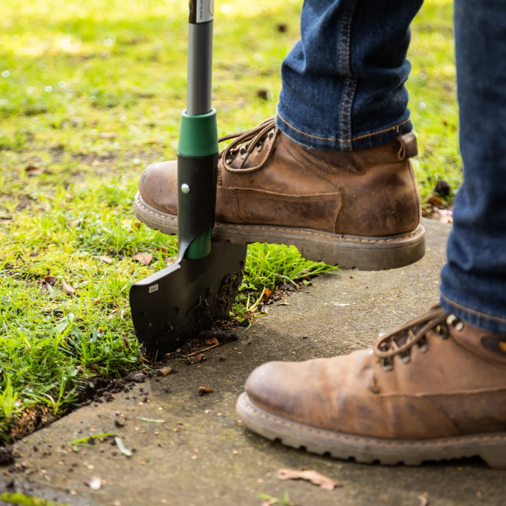 manual lawn edger cutting neat grass edge beside concrete sidewalk for yard maintenance