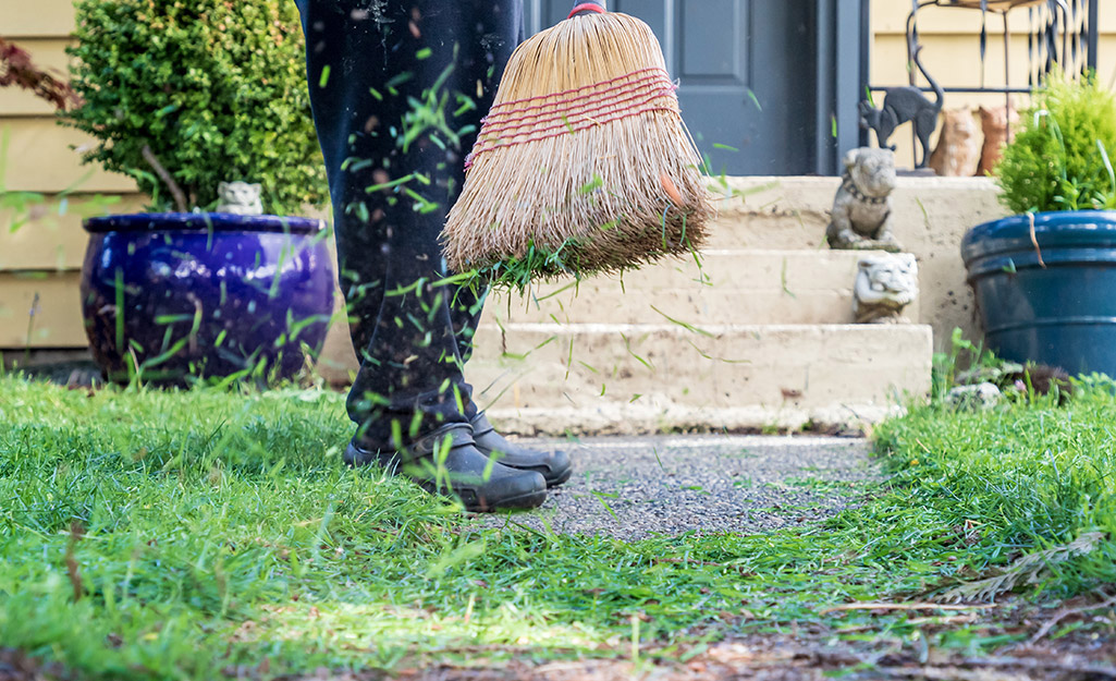person sweeping grass clippings after lawn edging near front steps and garden path