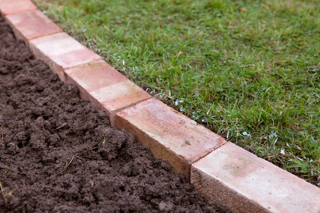 brick garden border edging installed beside lawn with fresh soil for landscape design