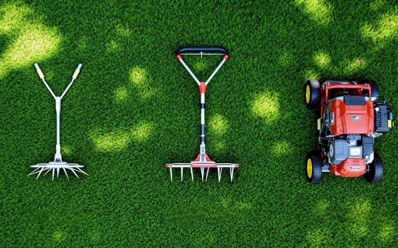 Top down view of three aeration tools side by side on a very green lawn. the left two are different manual aerators while the right most one is a gas powered tool.