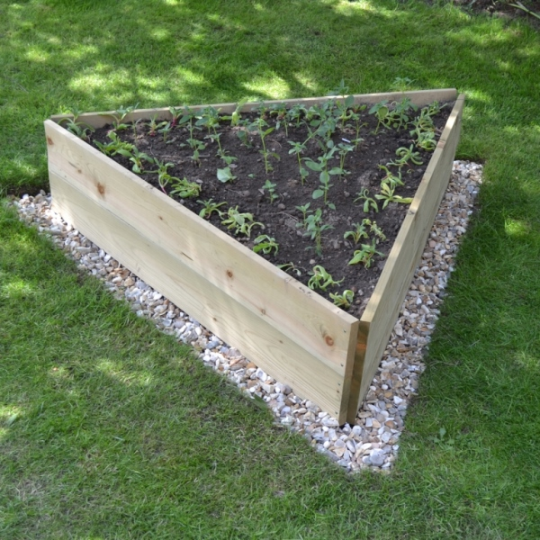 A triangular shaped raised garden with newly sprouted plants surrounded by pebbles in a lawn.