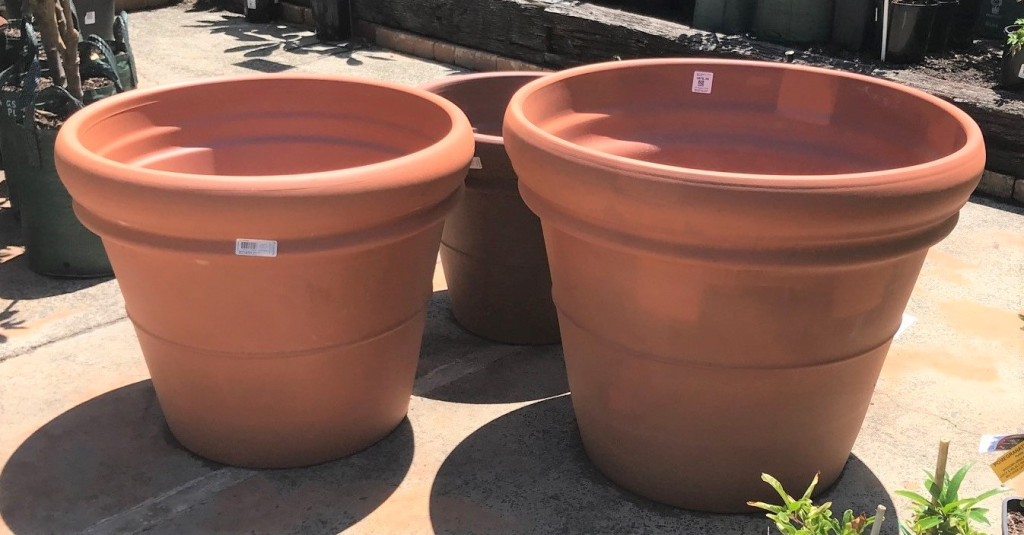 Three various sized empty terracotta pots on the concrete floor.