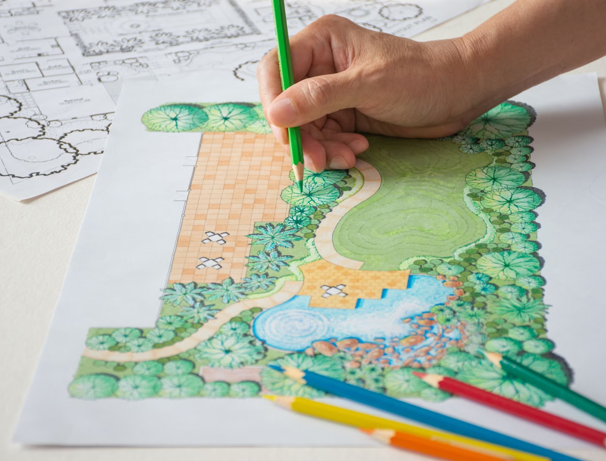 A hand holding a green crayola coloring pencil finalizing a garden draft on a white tabletop.