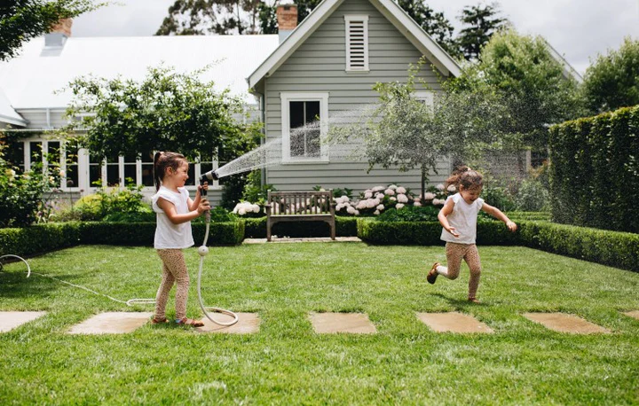 Two little girls playing on a lawn with a garden hose