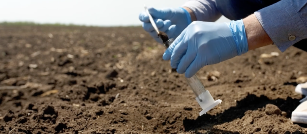 Gloved hands taking a dirt sample from land.