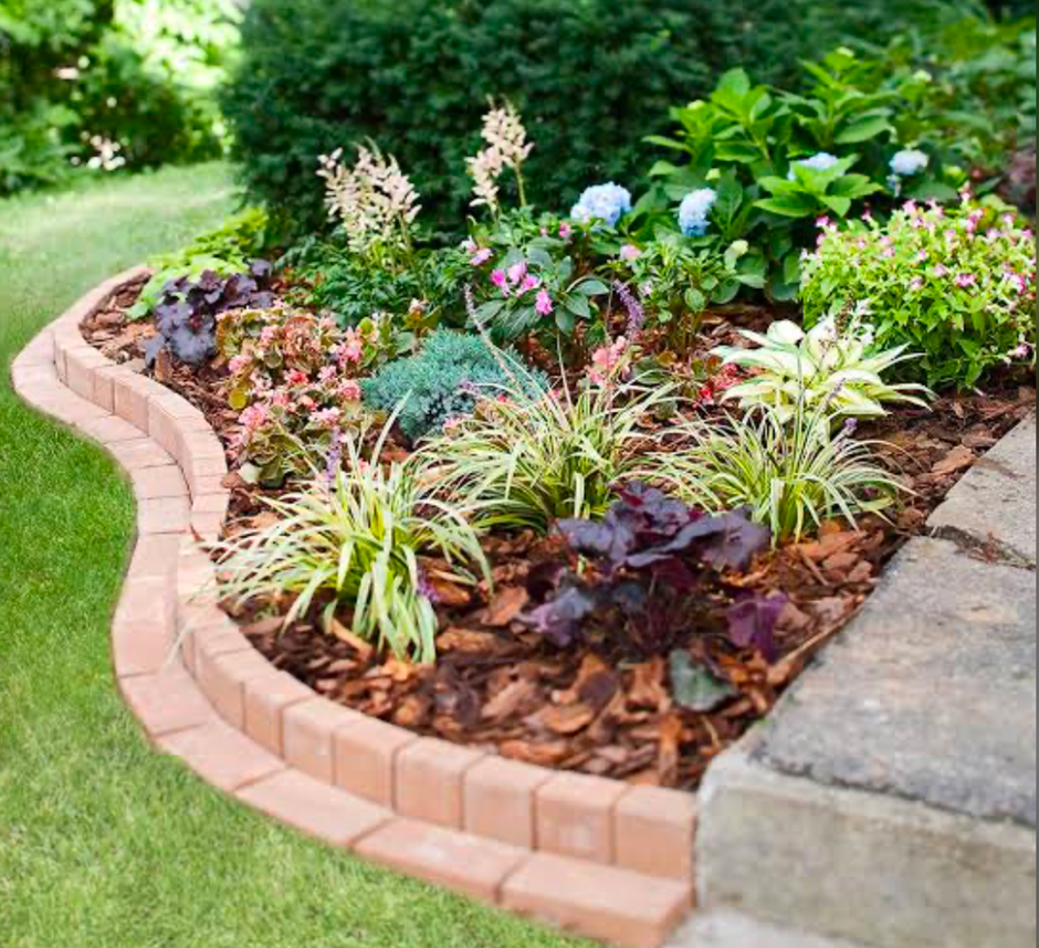 Mulched flower bed with brick edging and mixed perennials in a neat yard.