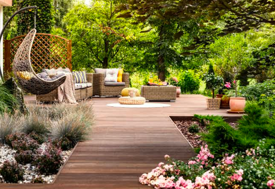 Backyard deck with outdoor seating, hanging chair, and lush garden borders.