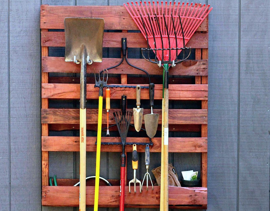 A stained red pallet reused as a gardening tool holder.