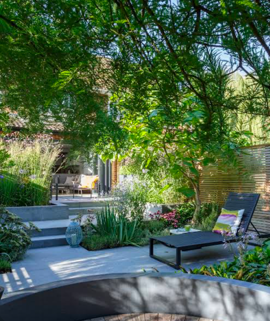Modern backyard garden with lounge chair, layered greenery, and shaded patio