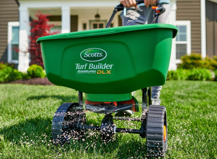 A Scotts Turf Builder drop spreader being pushed along a lawn spreading fertilizer.