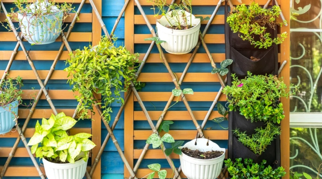 Vertical trellis garden with hanging pots and fabric planters filled with green foliage.