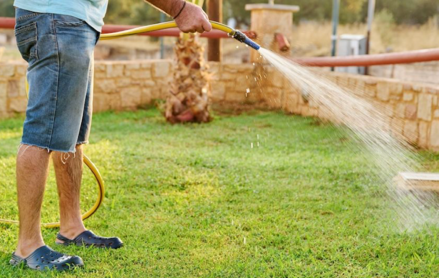 watering lawn with garden hose to support new grass seed growth