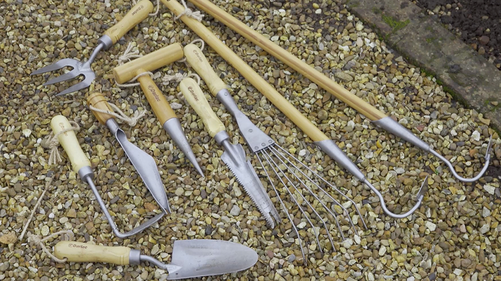 Wood-handled hand gardening tools arranged on gravel for traditional garden work