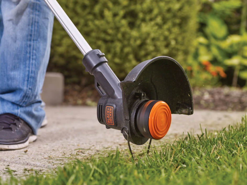 An individual walking along the sidewalk to their home trimming the edges of their lawn.