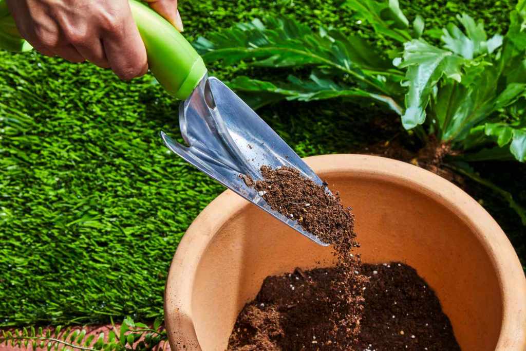 Hand using a garden trowel to add potting soil into a terracotta plant pot