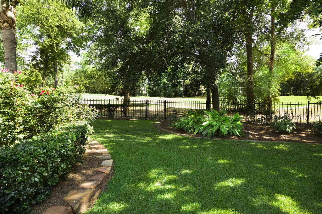 Landscaped backyard garden with healthy green lawn, trees, shrubs, and curved stone edging