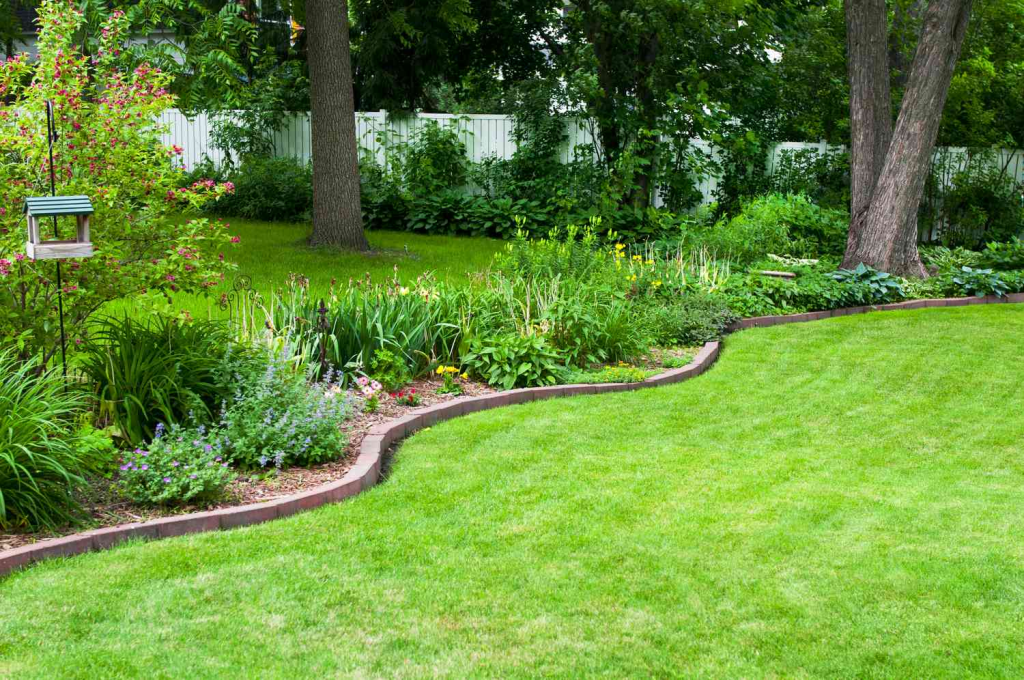 Landscaped backyard with curved flower bed border, mature trees, and healthy green lawn