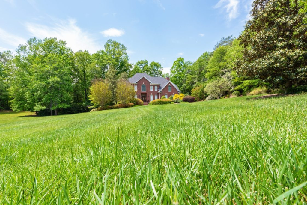 wide view of lush green lawn in front of a large house surrounded by trees