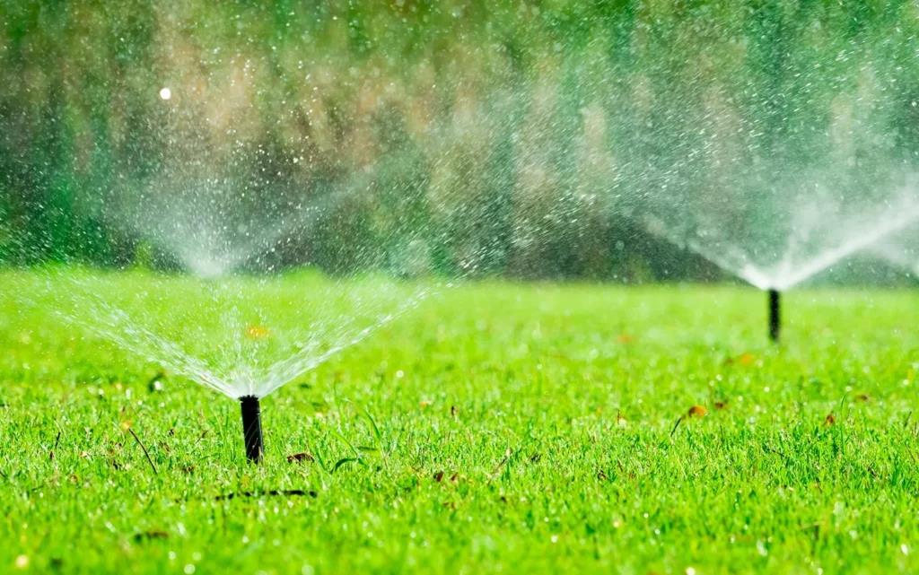 Lawn sprinkler spraying water in a lush green yard, creating a misty arc