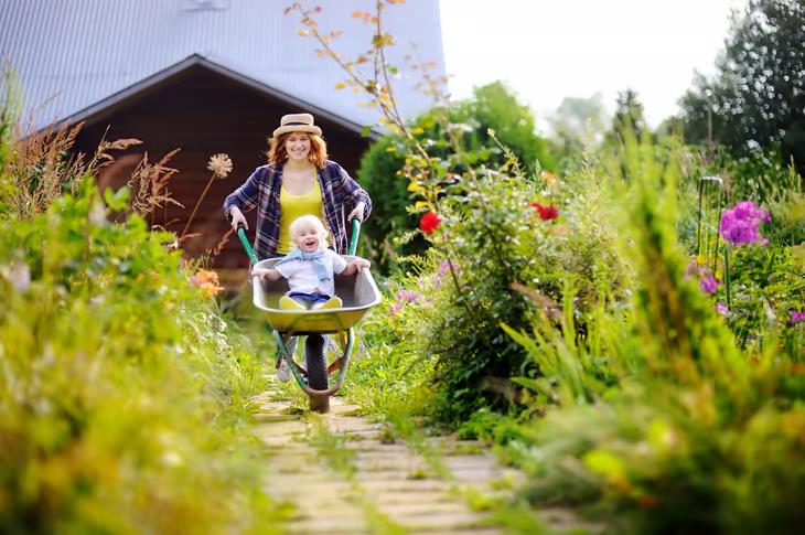 Smiling woman pushing child in a wheelbarrow through garden