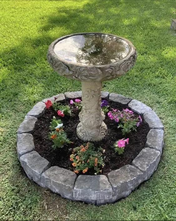Stone birdbath surrounded by colorful flowers and bricks.