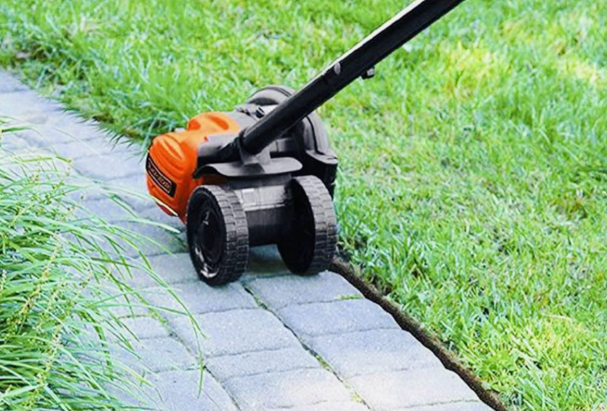 A lawn edger being used to cut the edge of a lawn between a paved pathway.