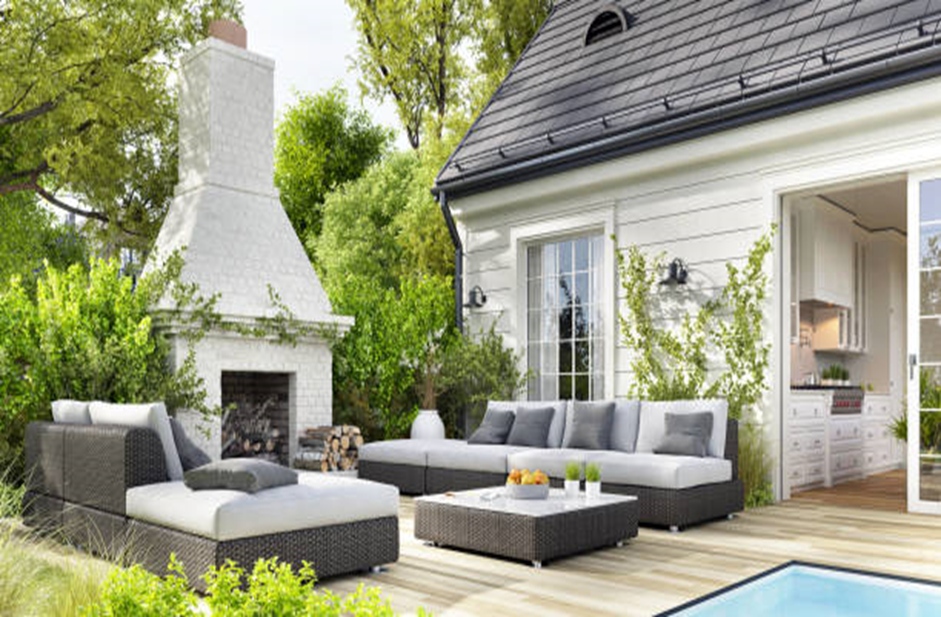 Modern backyard patio with white brick outdoor fireplace, wicker sectional, and poolside deck.