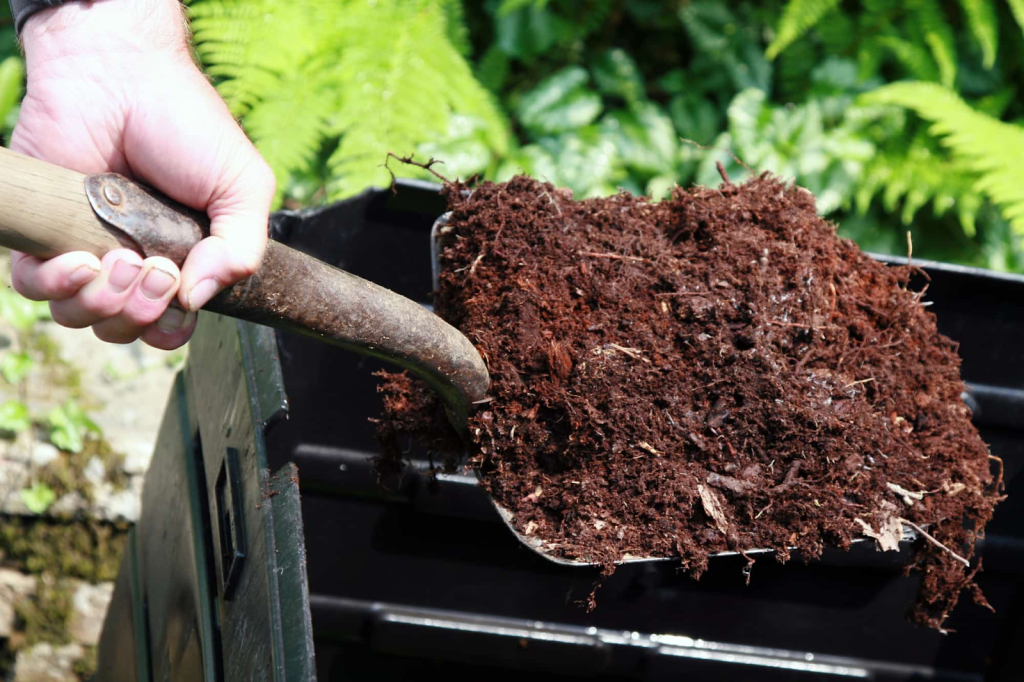 A gardener with soil on a shovel taken from a bin.