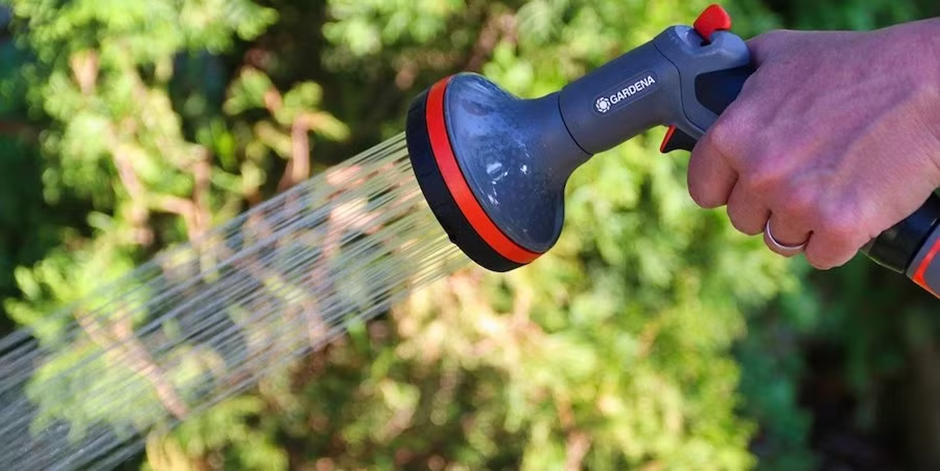 Hand holding a garden spray nozzle watering plants outdoors.