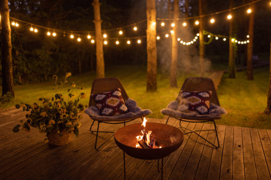 Cozy backyard patio at night with string lights, fire pit, and two cushioned lounge chairs.
