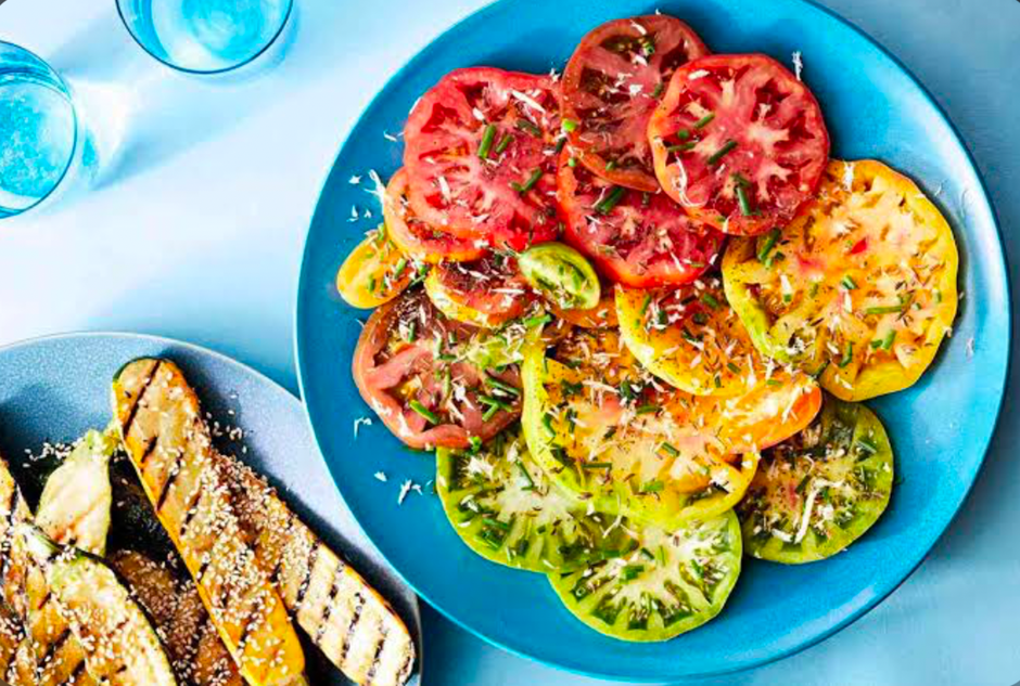 Sliced heirloom tomato salad with herbs on a blue plate and grilled zucchini.