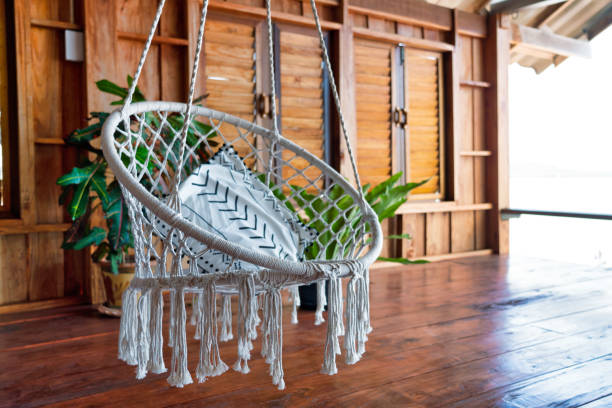 A beautiful white indoor chair swing is strung across this open wooden deck in a log cabin.  