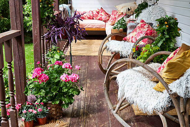 A modern-style summer veranda interior decorated with bright summer flowers, rattan rocking chairs, and a large pink sofa.