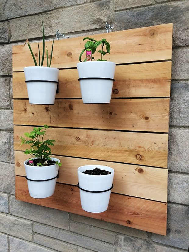 A repurposed pallet affixed to a brick wall with wires being used to hold white planters.