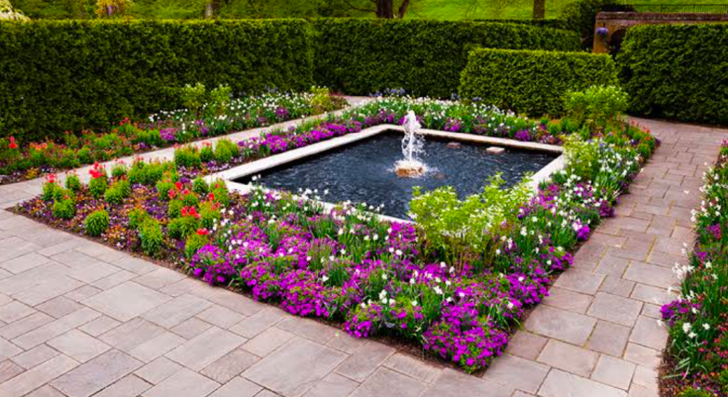 Symmetrical garden with central fountain surrounded by colorful flower beds and clipped hedges