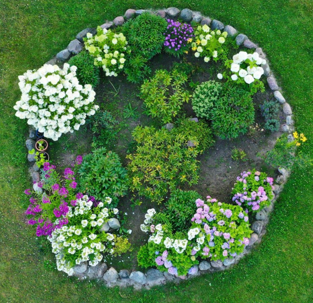 Circular flower garden bed with mixed shrubs and colorful blooms bordered by stones