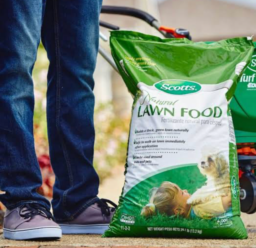 Bag of Scotts natural lawn food fertilizer next to lawn care equipment outdoors