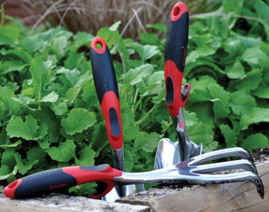 hand trowel and garden fork with red handles placed in raised garden bed