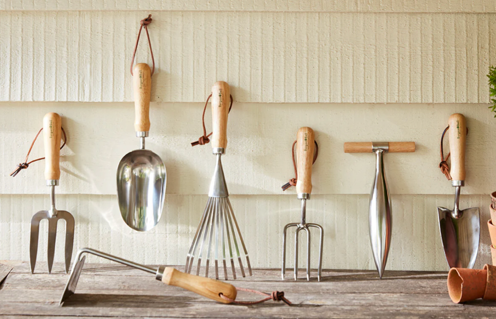 garden tools with wooden handles hanging on a wall including trowel, fork and rake