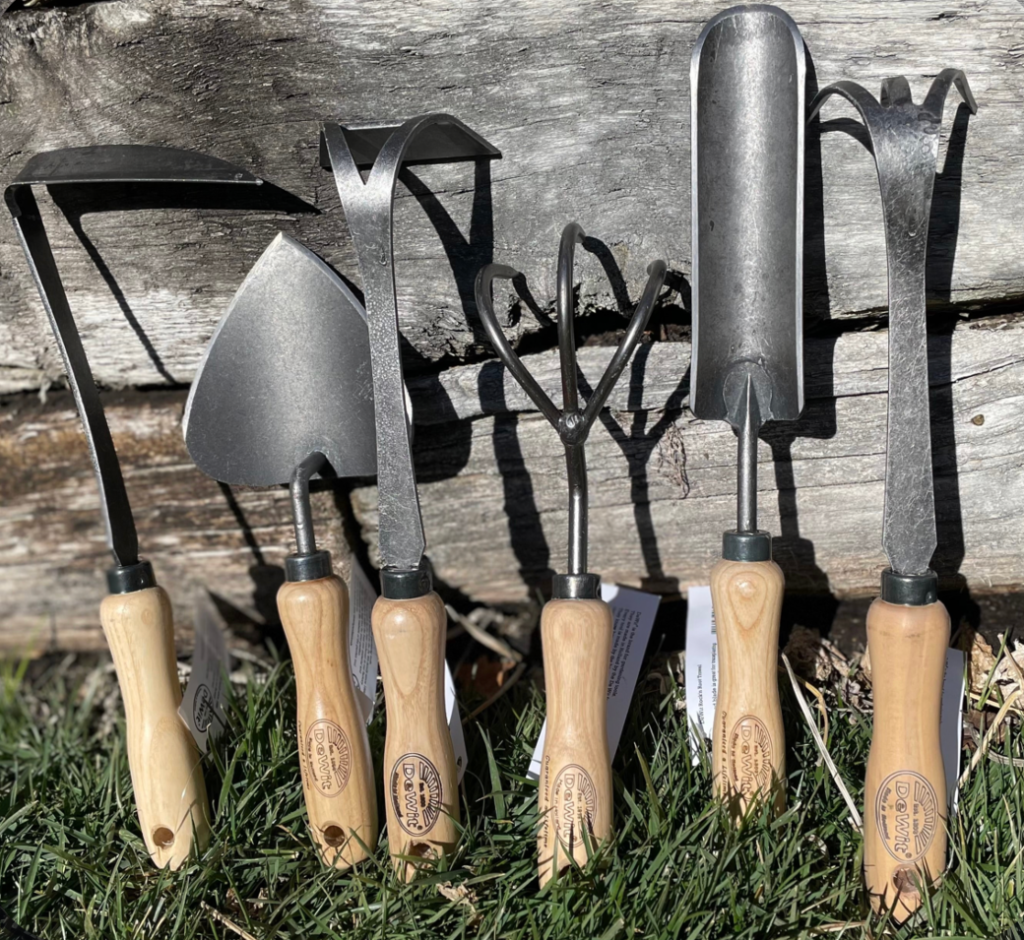 set of black steel garden tools with wooden handles standing in grass