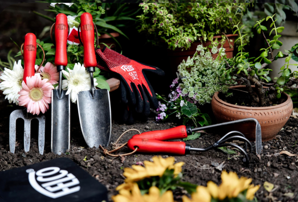 red handled garden tools and gloves arranged beside potted plants and flowers